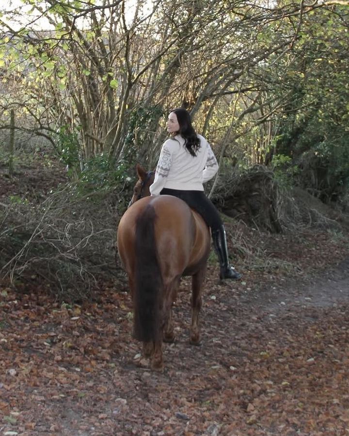 Hannah-Grace riding a chestnut horse along a leafy woodland path, looking back over her shoulder