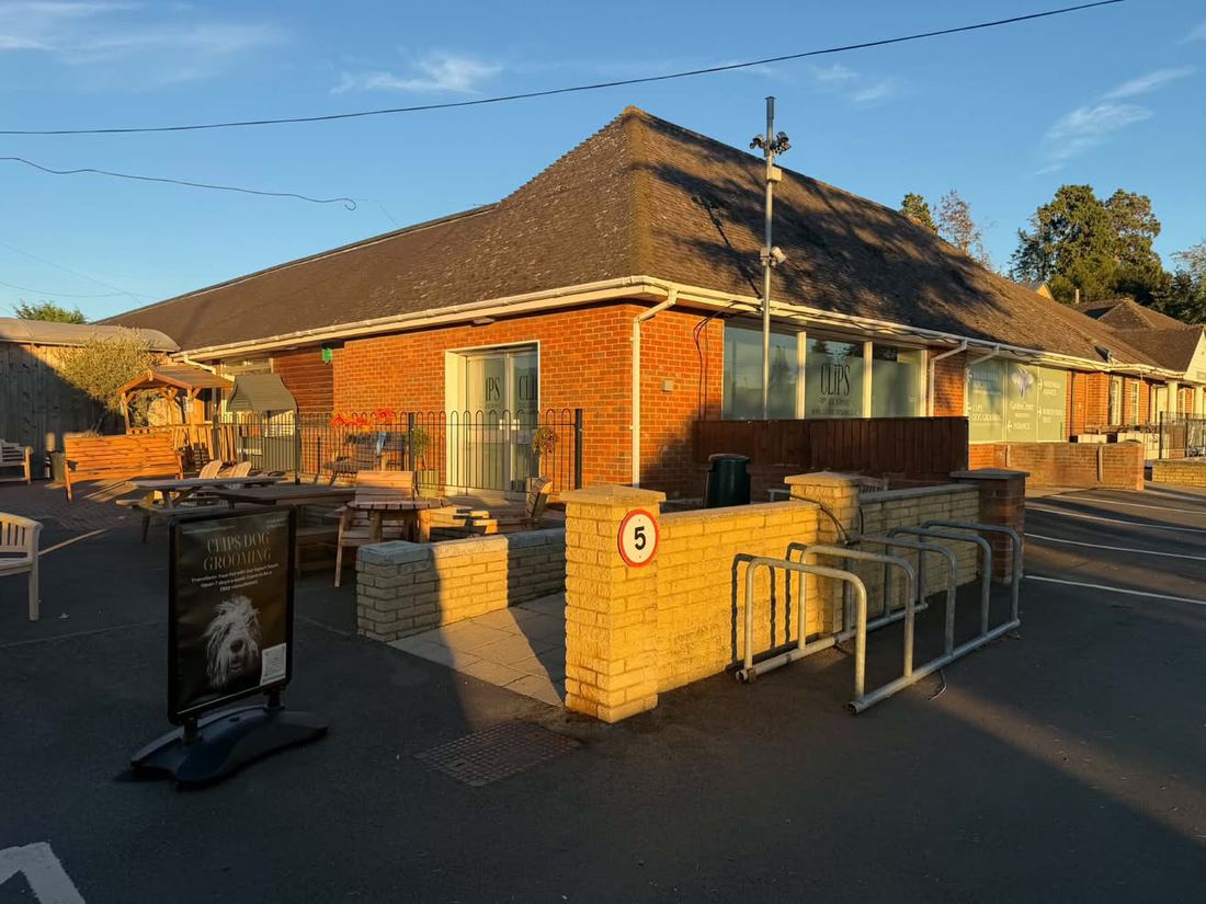 Red-brick single-storey building with a car park, outdoor seating and a Clips Dog Grooming sign